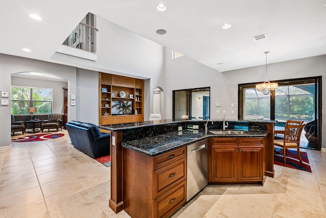 kitchen featuring stainless steel dishwasher, sink, a kitchen island with sink, dark stone countertops, and an inviting chandelier