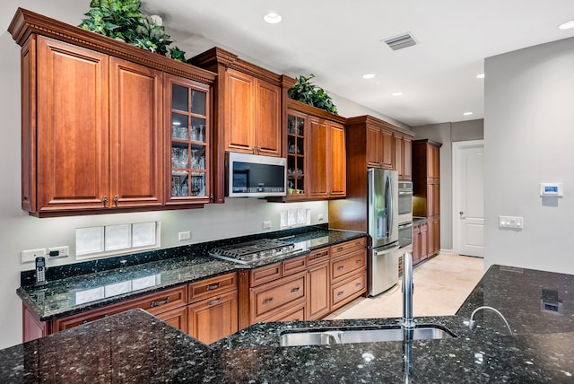 kitchen with light tile floors, appliances with stainless steel finishes, dark stone counters, and sink