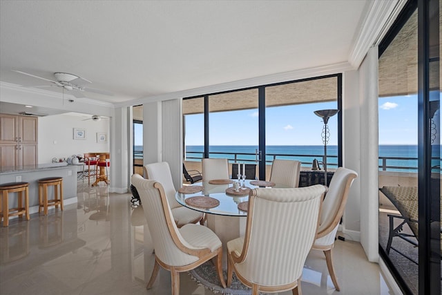 dining area featuring ornamental molding, a wall of windows, ceiling fan, and a water view