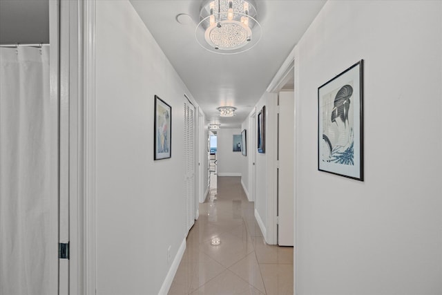 corridor featuring an inviting chandelier and light tile floors