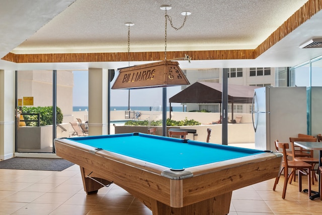 playroom with pool table, a tray ceiling, a water view, light tile floors, and a textured ceiling