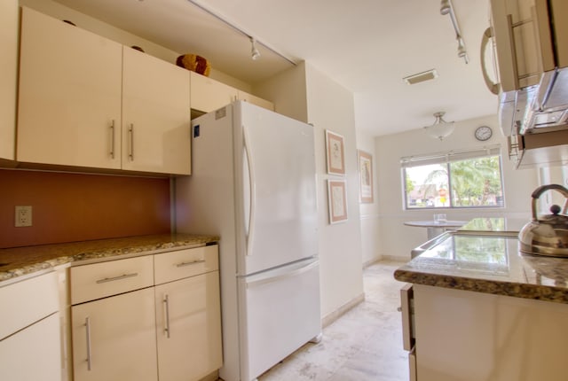 kitchen featuring white fridge, track lighting, white cabinetry, and light stone counters