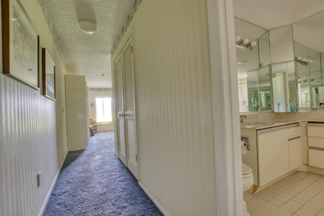 corridor with a textured ceiling, sink, and light carpet