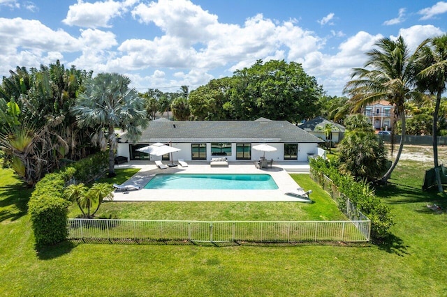 rear view of house with a fenced in pool, a lawn, and a patio area