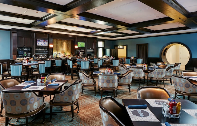 carpeted dining room with crown molding, beam ceiling, coffered ceiling, and bar area