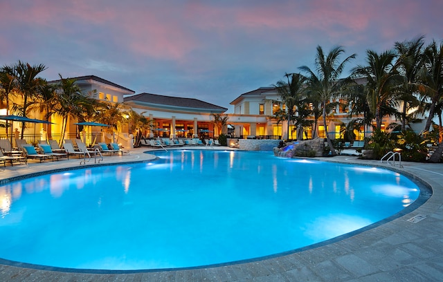 pool at dusk with pool water feature and a patio