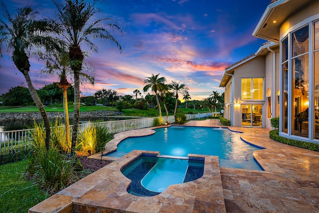 pool at dusk with an in ground hot tub and a patio