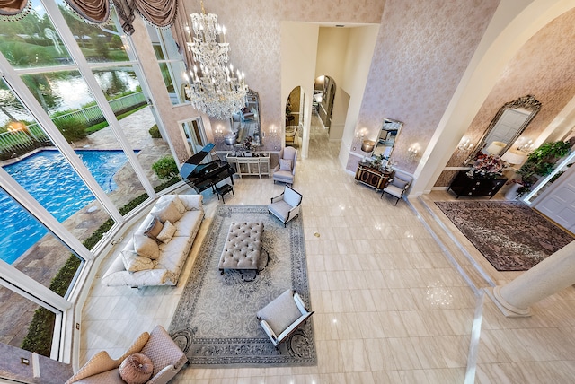 living room featuring an inviting chandelier, a towering ceiling, ornate columns, and light tile flooring