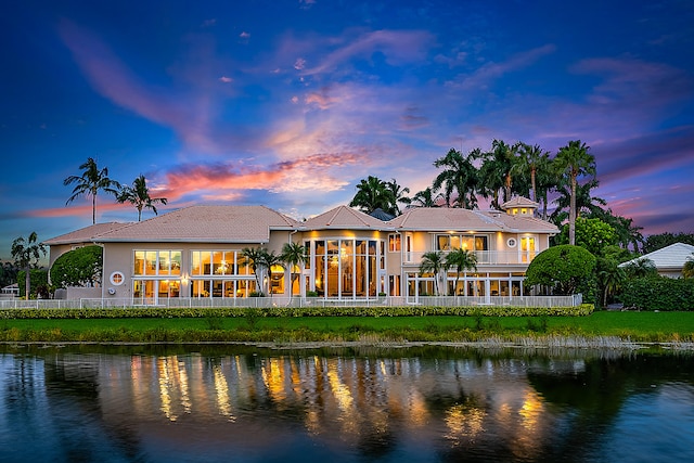 back house at dusk featuring a water view and a yard