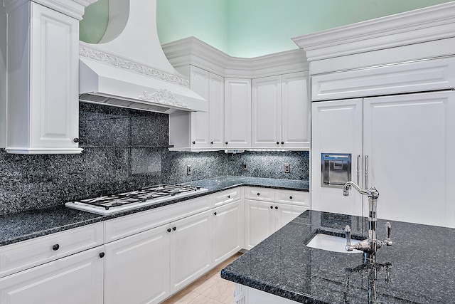 kitchen with white cabinets, backsplash, paneled fridge, and custom exhaust hood