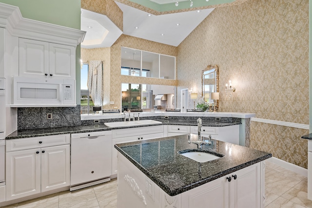 kitchen with an island with sink, white appliances, a towering ceiling, and white cabinetry