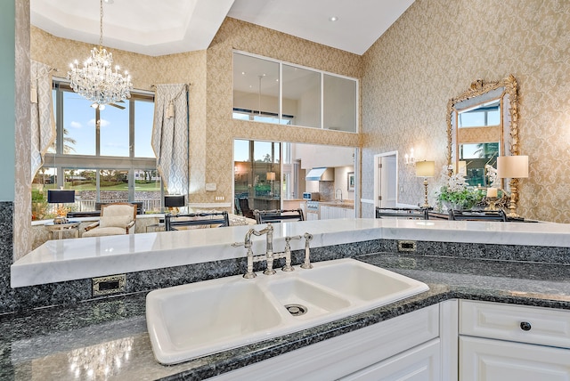 bathroom featuring plenty of natural light, a tray ceiling, a notable chandelier, and vanity with extensive cabinet space