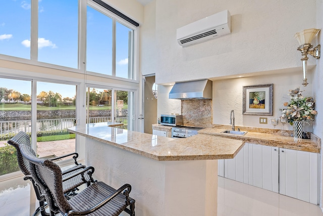 kitchen with wall chimney range hood, light tile flooring, a high ceiling, a breakfast bar area, and sink