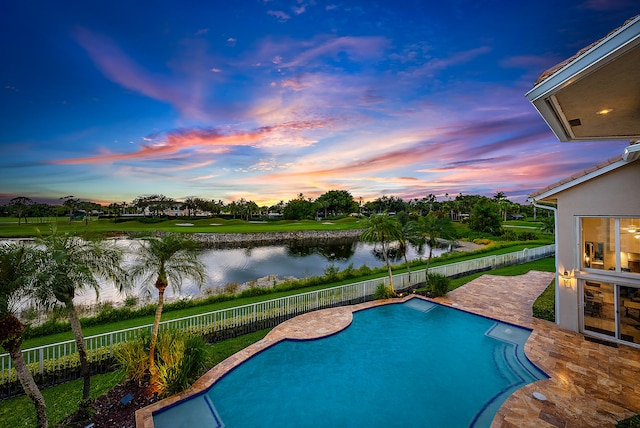 pool at dusk featuring a water view and a patio