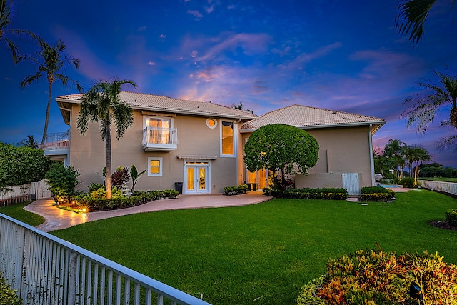 view of front of home featuring a balcony, french doors, and a yard