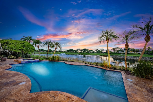 pool at dusk with an in ground hot tub and a water view