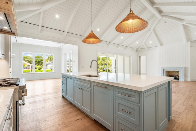 kitchen featuring high end range, open floor plan, gray cabinetry, light wood-type flooring, and a sink