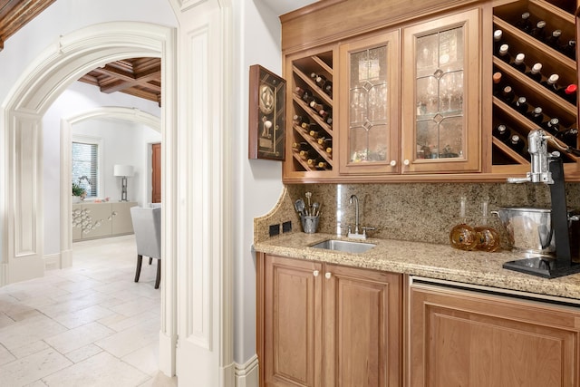 bar with light stone countertops, coffered ceiling, sink, tasteful backsplash, and crown molding