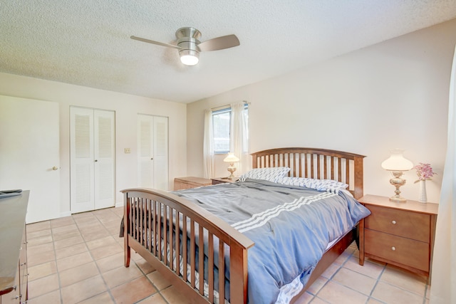 bedroom with light tile patterned floors, a textured ceiling, ceiling fan, and multiple closets