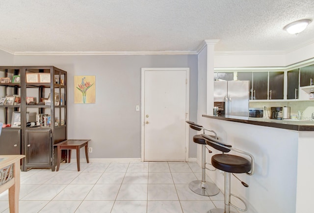 kitchen featuring stainless steel fridge, light tile patterned floors, a textured ceiling, and ornamental molding