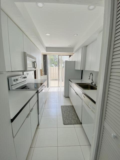 kitchen featuring white appliances, white cabinets, sink, and light tile flooring