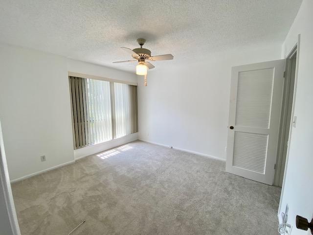 empty room with light colored carpet, ceiling fan, and a textured ceiling