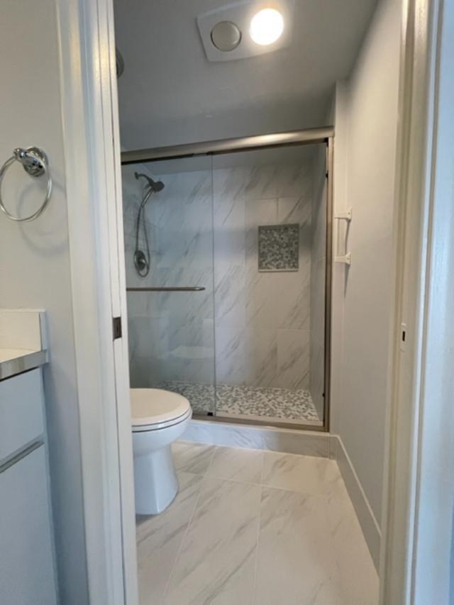 bathroom featuring walk in shower, tile floors, toilet, and vanity