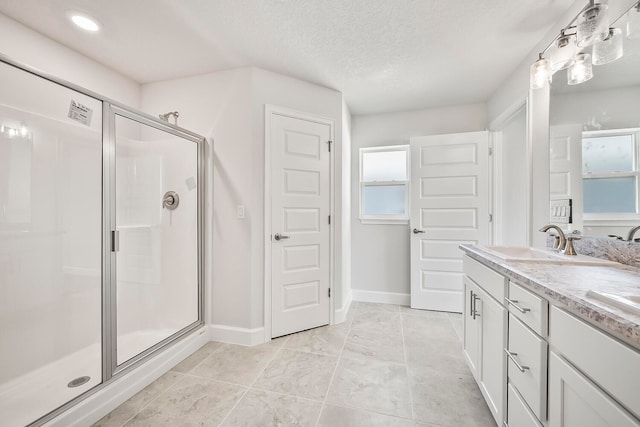 bathroom with a textured ceiling, a shower with shower door, vanity with extensive cabinet space, and tile flooring