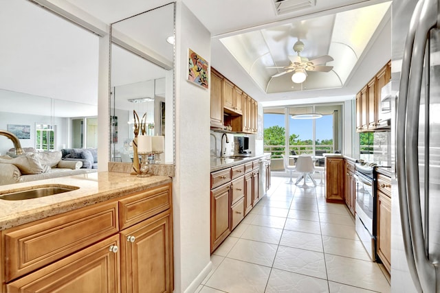 kitchen featuring stainless steel fridge, light stone counters, light tile patterned floors, ceiling fan, and sink