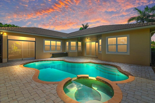 pool at dusk featuring an in ground hot tub and a patio