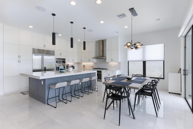 kitchen featuring white cabinetry, hanging light fixtures, stainless steel appliances, wall chimney range hood, and a spacious island