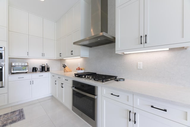 kitchen featuring decorative backsplash, white cabinetry, stainless steel gas stovetop, and wall chimney exhaust hood