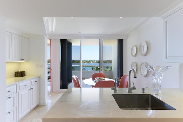 kitchen with white cabinetry, ornamental molding, sink, and a wall of windows