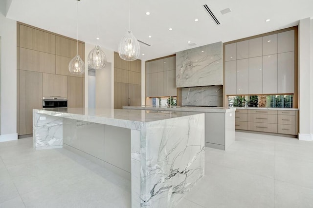 kitchen with a large island, light stone countertops, oven, decorative light fixtures, and light brown cabinetry