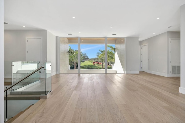 empty room with light hardwood / wood-style floors, a healthy amount of sunlight, and a wall of windows