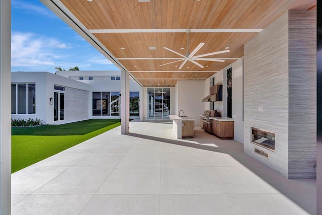 view of patio featuring a large fireplace, ceiling fan, sink, exterior kitchen, and grilling area