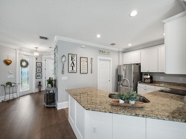 kitchen with dark stone countertops, ornamental molding, sink, stainless steel fridge, and white cabinetry