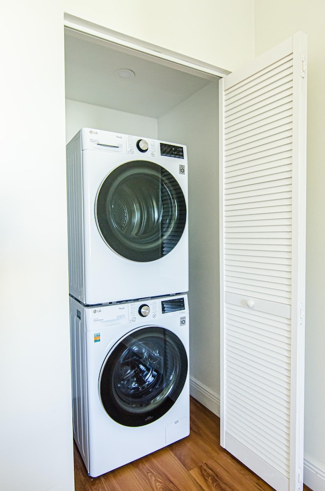 laundry area featuring stacked washer / drying machine and dark hardwood / wood-style flooring