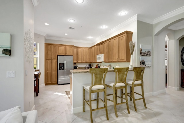 kitchen with light tile floors, light stone countertops, stainless steel fridge with ice dispenser, a breakfast bar area, and crown molding