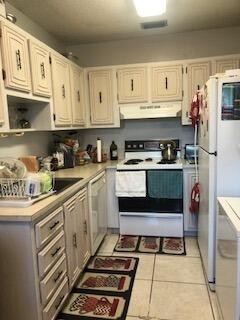 kitchen with white appliances, white cabinetry, light tile floors, and ventilation hood