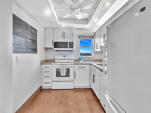 kitchen with light wood-type flooring, white cabinetry, backsplash, a raised ceiling, and white appliances