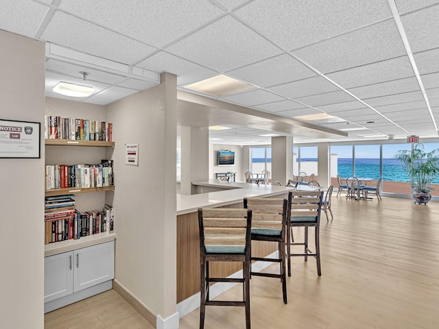 kitchen with light hardwood / wood-style floors, a breakfast bar, kitchen peninsula, a drop ceiling, and white cabinets