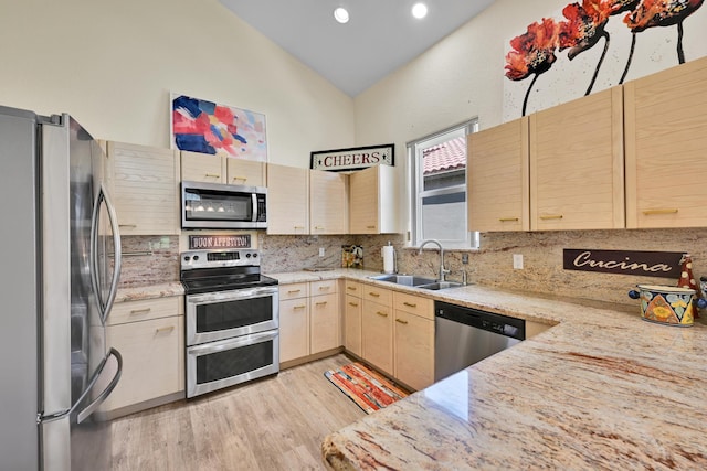 kitchen with light brown cabinetry, light wood-style floors, tasteful backsplash, a sink, and appliances with stainless steel finishes