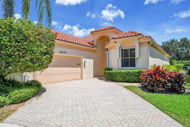 mediterranean / spanish home featuring a garage, stucco siding, a tile roof, and decorative driveway