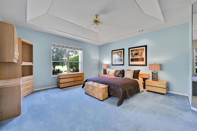 carpeted bedroom featuring a tray ceiling, ceiling fan, and baseboards
