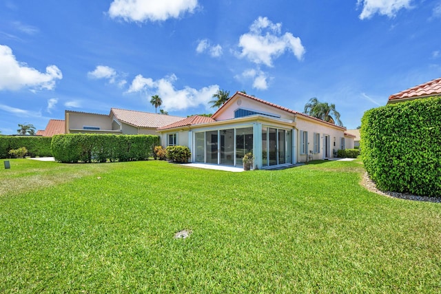 back of property with a lawn, stucco siding, a sunroom, and a tile roof