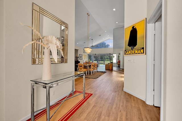 corridor featuring baseboards, recessed lighting, high vaulted ceiling, and wood finished floors