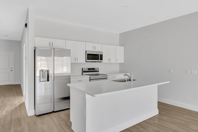 kitchen with sink, stainless steel appliances, light hardwood / wood-style floors, white cabinets, and a center island with sink