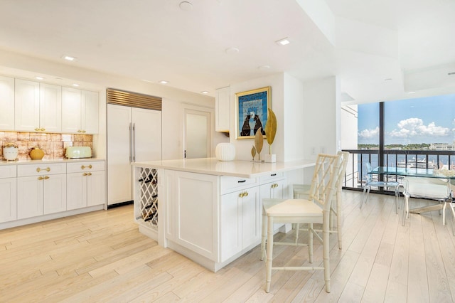 kitchen with a wall of windows, built in fridge, white cabinets, backsplash, and light wood-type flooring