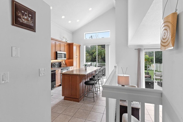 kitchen featuring light tile patterned floors, a kitchen breakfast bar, stainless steel appliances, a kitchen island, and dark stone counters